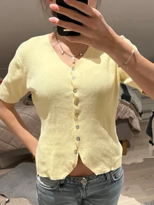 Gul kortärmad topp med pärlknappar - Säljer en gammal vintage gul tröja. Skönt material och inga tecken på slitage. Passar perfekt till jeans eller en kjol!