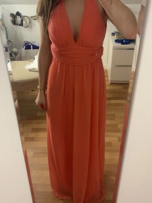 Korallfärgad långklänning NLY Eve - Säljer en snygg korallfärgad bal/fin klänning från NLY Eve i storlek 34. Klänningen har djup v-ringning, bred midjedetalj och faller snyggt i ett lätt, flytande tyg. 