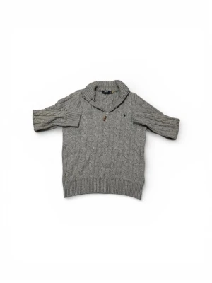 Grå kabelstickad tröja Polo Ralph Lauren - Kabelstickad grå tröja från Polo Ralph Lauren med halv dragkedja och hög krage. Klassisk broderad logga på bröstet. Tröjan är långärmad och har ribbade muddar vid ärmslut och nederkant. Perfekt för kyliga dagar.