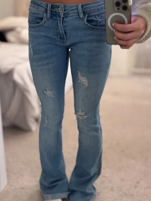 Blå lågmidjade flare jeans - Säljer ett par superfina blå jeans i lågmidjad modell med lätt utsvängda ben. Sitter jättebra och är stretchiga och bekväma. Slitna detaljer framtill som ger en snygg look🥰