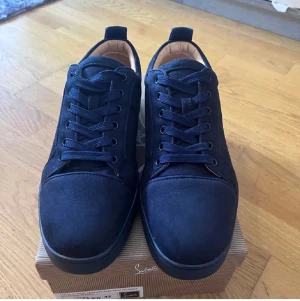 Mörkblå sneakers från Christian Louboutin - Snygga mörkblå sneakers från Christian Louboutin i mocka med klassisk röd sula och rund tå. Skorna har snörning och beige innersida i skinn. Perfekta för dig som vill ha en lyxig och stilren look med en ikonisk touch. Ingen skoho 