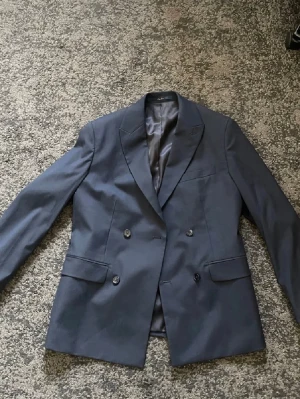 Dubbelknäppt kavaj mörkblå - Säljer en dubbelknäppt mörkblå kavaj från Mango i storlek 48 slim fit. Nypris är 1499 kr. Kavajen är bara använd en gång och är i perfekt skick. 