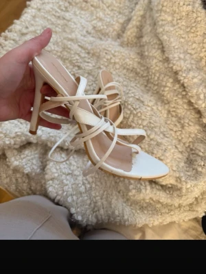 Vita strappy klack-sandaler - Säljer ett par vita sandaler med smala remmar och hög klack från NA-KD. Skorna har spetsig tå och flera tunna remmar som korsar foten för en trendig look. Perfekta för dig som gillar stilrena och moderna skor.