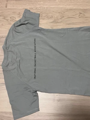 Grå NBA t-shirt från Zara - Snygg grå t-shirt från Zara med tryck   Av NBA på framsidan och liten text där back. Inga hål m.m på den. st 164