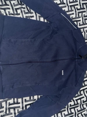 Marinblå mjukisbyxor från BOSS - Mörkblå mjukisbyxor från BOSS med vit snörning i midjan och diskret logga på vänster höft. Byxorna har muddar vid bensluten och är tillverkade i mjukt material som passar perfekt för en avslappnad stil.