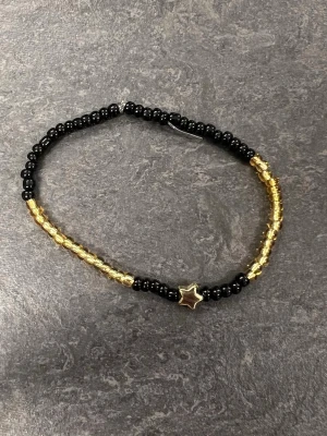 Pärlarmband med stjärna svart/guld Storlek M  - Armband med svarta och guldiga pärlor samt en stjärnformad detalj i mitten. 