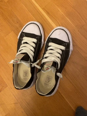 Svarta sneakers från MMY - Svarta sneakers från MMY med vit sula och vita snören. Klassisk design med rund tå och tydliga kontrastsömmar. Märkeslapp på plösen med textdetaljer. Perfekta för en avslappnad och trendig stil.