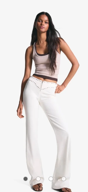 Vita utsvängda jeans med nitar - Snygga vita jeans med utsvängda ben och coola silverfärgade nitar längs linningen. Hög midja och klassisk femficksmodell. Perfekta för dig som vill sticka ut med en trendig och fräsch look. Jeansen är från Bershka, slutsålda, helt nya köpa enbart provade. Kommer inte komma till användning tyvärr. Skulle säga att beroend epå preferns funkar de för en s-m