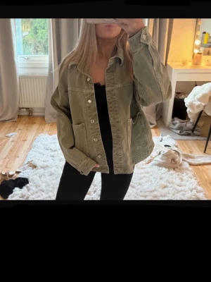 Jeansjacka  - Snygg olivgrön jeansjacka med oversized passform och stora fickor framtill. Jackan har klassisk krage, knäppning med silverfärgade knappar och raka ärmar. Perfekt för en avslappnad och trendig look.