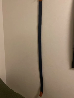 Mörkblå flätat bälte med läderdetaljer - Snyggt mörkblått flätat bälte med bruna läderdetaljer och silverfärgat spänne. Bältet har storlek 85 och passar perfekt till jeans eller chinos för en stilren look.