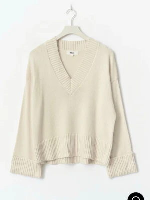 Beige stickad tröja med v-ringning - Säljer en beige stickad tröja från Gina med djup v-ringning och breda ribbade muddar vid ärmslut och nederkant. Tröjan har en avslappnad passform och är tillverkad i mjukt material, perfekt för lager på lager under kyliga dagar.