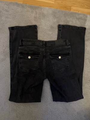 Svarta jeans från 157 - Säljer ett par svarta jeans från 157 med raka ben och klassisk femficksmodell. Jeansen har silverfärgade knappar och nitar samt ficklock på bakfickorna. De är lågmidjade/midwaist. Skriv för fler frågor, bilder eller prisförslag🥰