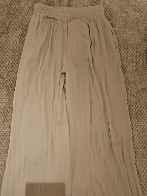Beiga vida linnebyxor från Zara - Säljer ett par beiga linnebyxor från Zara med avslappnad passform och resår i midjan. Byxorna är vida och har en mjuk, luftig känsla som passar perfekt till sommaren. Materialet är lätt och ger en skön vibe till din outfit.