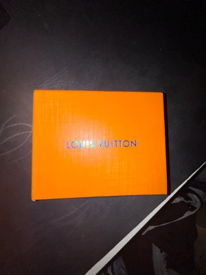 Svart Läder monogram plånbok - Snygg svart plånbok  med klassisktmonogrammönster i grått. Tillverkad i läder och levereras i original orange box. Perfekt för dig som vill ha en stilren och lyxig accessoar i fickan.