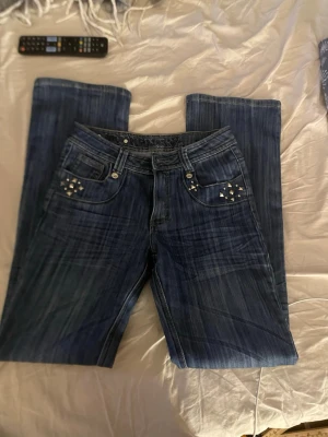 Blå bootcut jeans med nitar - Säljer ett par blå bootcut jeans från YOU YIPIN  med coola nitar och dekorsömmar på fickorna. Jeansen har klassisk femficksmodell och snygg tvättad look. Perfekta för dig som vill ha en unik och trendig stil.  Jag är lite osäker på storleken då det inte står, men jag väger ca 55 kg och är 167 och de sitter bra på mig och är lite långa, skulle nog passa någon som är 170 eller en kortare person om man syr upp de eller gillar att ha långa byxor