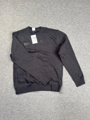 Svart Nike AIK sweatshirt - Svart sweatshirt från Nike med AIK-brodyr på bröstet. Klassisk rund halsringning och ribbade muddar vid ärmslut och nederkant. Perfekt för dig som gillar sportig stil och vill representera AIK. Tillverkad i mjukt material för skön känsla.