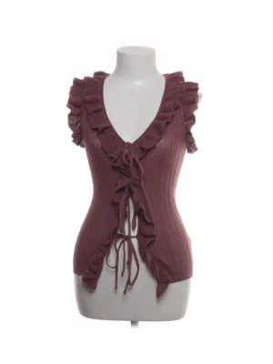 Ribbad volangtopp från Zara - Superfin ribbad topp från Zara i en röd färg. Toppen är ärmlös med volangdetaljer längs v-ringningen och framtill, samt snörning som knyts framtill. Perfekt för dig som vill ha något unikt och trendigt.