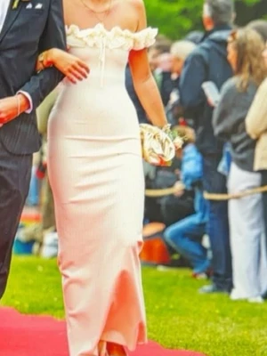 Vit långklänning med volang - Supersnygg vit långklänning från Positano med offshoulder och volangdetaljer runt axlarna. Klänningen har snörning framtill och är figurnära med en elegant siluett. Perfekt till balen!