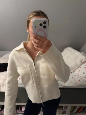 Vit stickad ziptröja med krage - Snygg vit trendig tröja med dragkedja framtill och två stora bröstfickor. Tröjan har en klassisk krage och raka ärmar. Säljer då den inte kommer till användning köpte på Åhléns för 599kr nypris. Jag är 166cm lång och bär storlek S. Kom med prisförslag. Den är använd fåtal gånger men det är inget som syns den är i väldigt fint skick