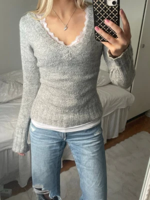 Grå stickad tröja med v-ringning - Säljer en ljusgrå stickad tröja med djup v-ringning och ribbade muddar. Tröjan har en figurnära passform och långa ärmar. Perfekt att matcha med ett linne under för en snygg lager-på-lager-look. Typisk S skulle jg säga.