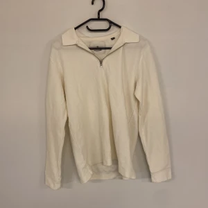Jack Jones zip - Vit långärmad topp från Jack & Jones med klassisk krage och halv dragkedja framtill. Enkel och stilren design i mjukt bomullsmaterial, perfekt för en clean och avslappnad look.
