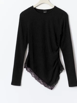 Svart långärmad topp med spetskant - Säljer en svart långärmad topp från Gina Tricot med asymmetrisk nederkant och snygg spetsdetalj. Toppen är ribbad och har en figurnära passform som ger en trendig look. Perfekt att styla med jeans eller kjol för en cool vibe.