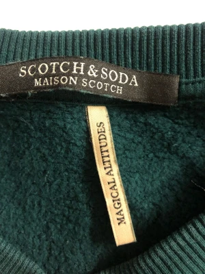 Mörkgrön sweatshirt Scotch & Soda - Mörkgrön sweatshirt från Scotch & Soda med rund halsringning och ribbade muddar. Framsidan har ett stort tryck med ordet 'Love' i ljusare grönt. Tillverkad i mjukt material för en chill och trendig look.