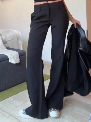 Svarta utsvängda kostymbyxor - Snygga svarta kostymbyxor från venderbys med medelhög midja och utsvängda ben. Klassisk design med hällor för skärp och diskreta fickor. Perfekta för en trendig och stilren look. Modellen Livia. Säljer då jag beställde en för stor storlek så aldrig använda💕lånade bilder