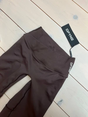 Bruna seamless leggings från DFYNE - Snygga bruna seamless leggings från DFYNE med hög midja och bred linning. Tillverkade i ett stretchigt material som sitter skönt och formar sig efter kroppen. Perfekta för träning eller chill. Diskret logga på linningen och stilren design.