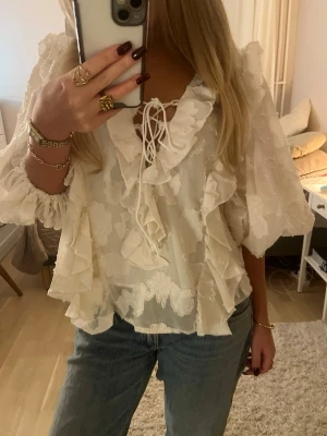 Vit volangblus med knytning - Säljer en vit blus med volanger och broderade blommor. Blusen har v-ringning med knytband och trekvartsärmar med resår vid ärmslut. Den är helt oanvänd. Materialet känns lätt och luftigt.❤️