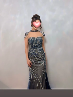 Blå långklänning med pärldetaljer - Elegant långklänning i marinblått med gnistrande pärldetaljer och broderade mönster. Perfekt för bal eller festliga tillfällen.