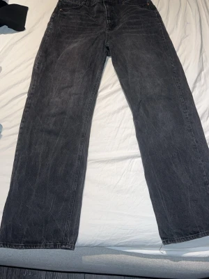 Svarta raka jeans med vintagekänsla - Säljer ett par svarta jeans med rak passform och lätt tvättad vintage-look. Jeansen har klassisk femficksdesign och är tillverkade i kraftigt denimtyg. Perfekta för en avslappnad och trendig stil.