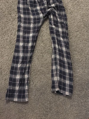 Rutiga pyjamasbyxor i bomull - Mysiga pyjamasbyxor med svart, vitt och grått rutmönster. Tillverkade i mjuk bomull med avslappnad passform och långa ben. Perfekta för chillkvällar hemma.