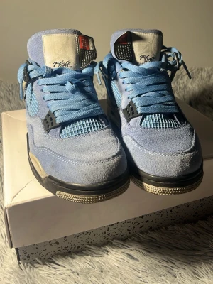 Air Jordan 4 University Blue sneakers - Kan diskutera Pris!!! Snygga Air Jordan 4 University Blue sneakers med ljusblå mocka och mesh, svarta och grå detaljer samt klassisk Jumpman-logga på hälen. Skorna har snörning och en chunky sula med stänk i grått och svart. Perfekta för dig som gillar streetwear och vill sticka ut.