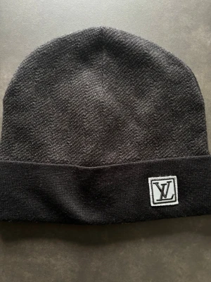 Svart mössa - Snygg svart mössa med uppvikt kant och finns logga framtill. Tillverkad i mjukt stickat material som håller dig varm och stilren under kalla dagar. Perfekt accessoar för dig som gillar exklusiva märken och enkel design. Priset kan diskuteras!