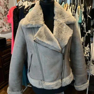 Grå fuskpälsjacka från Stradivarius - Säljer en grå fuskpälsjacka från Stradivarius i storlek M. Jackan har mjukt fuskpälsfoder, bred krage och detaljer med dragkedjor. Snygg och varm med en super fin passform, perfekt för kyliga dagar. Fickor med dragkedja och fluffiga kanter ger extra stil. Helt ny, har aldrig kommit till användning. Det finns en liten prick på ena armen som syns knappt, som jag hade inte märkt vid köpet.