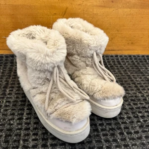 Beiga fluffiga boots med snörning - Supermysiga boots i beige med fluffig pälsimitation och tjock sula. Skorna har snörning framtill och är perfekta för kalla dagar när du vill hålla fötterna varma och snygga. Passar dig som gillar en trendig och cozy stil.