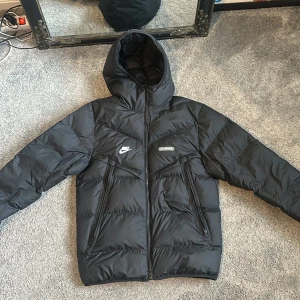 Svart Nike Air Max pufferjacka med huva - Säljer en svart pufferjacka från Nike Air Max med huva och dragkedja framtill. Jackan har två snedställda fickor med dragkedja, broderade loggor på bröstet och en cool detalj på ryggen. Perfekt för kalla dagar och riktigt street. Säljer eftersom jag inte använder den längre.(pris kan diskuteras)