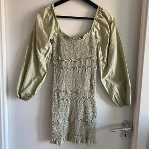 Ljusgrön smockad klänning Topshop 36 - Supersöt ljusgrön kortklänning från Topshop med smockad kropp, volangdetaljer och puffiga långärmar. Klänningen har en fyrkantig ringning. Storlek S