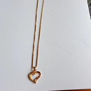 Guldhalsband med hjärthänge S835  - Snyggt halsband i guld med ett öppet hjärthänge dekorerat med små glittrande stenar. Kedjan är tunn och elegant, perfekt för att ge din look lite extra shine. Hängsmycket har en modern design med en böjd form och detaljer som gör det unikt. Kedjan är stämplad S835 men ser ingen stämpel på hjärtat men är fint ihop.rekommenderas för barn då kedjan mäter 38 cm.