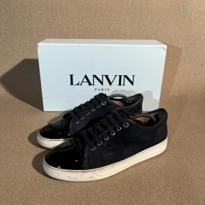 Lanvin dbb1 - Fräscha skor som går hem hela året runt. Den marinblåa färgen fungerar till varenda outfit.  Storlek: 41 EU | Färg: Marinblå | Skick: Bra skick (små repor på toe capen, skada på läder linjen av ena skon, några vatten skador på mockan) | Material: Mocka | Tillbehör: Box, Dustbag & Skosnörren | Pris: 2799kr | Dm för frågor.