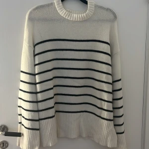 Vit randig stickad tröja 157 XS - Vit stickad tröja från 157 i storlek XS med svarta horisontella ränder. Tröjan har ribbade muddar och rund halsringning. Oversized fit med långa ärmar och mjukt material som passar perfekt till jeans eller kjol. Den har en liten fläck på armen, men går nog bort i tvätten.