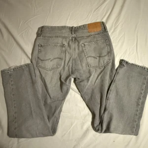 Jack&jones ljusgrå jeans straight fit - Ljusgrå Jack&jones. Jeansen har en snygg vintage-vibe med råa kanter vid benslut och ikonisk läderpatch bak i midjan. Tillverkade i slitstarkt bomullsjeansmaterial, perfekta för en chill och avslappnad stil.