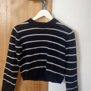 Randig svart stickad tröja H&M - Snygg svart stickad tröja från H&M med vita horisontella ränder. Tröjan har ribbad halsringning, muddar och nederkant samt lång ärm. Perfekt för dig som gillar en klassisk men trendig look.