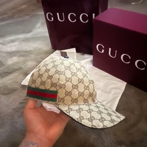 Gucci beige keps med GG-mönster - Exklusiv keps från Gucci i beige med klassiskt GG-monogram över hela kepsen. Perfekt för dig som vill ha en lyxig och trendig accessoar. Använt fåtal gånger.