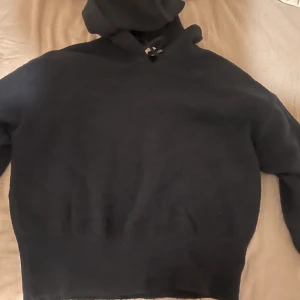 Svart stickad hoodie med huva - Mysig svart stickad hoodie med huva och snörning i halsen. Tröjan har ribbad nederkant och långa ärmar, perfekt för kyliga dagar. Enkel och stilren design som passar till det mesta.