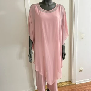 Ljusrosa långklänning med glittrig kant - Flowy ljusrosa långklänning med glittrande detaljer längs halsringningen och axlarna. Klänningen har en lös passform och är tillverkad i ett tunt, lätt material som ger ett elegant fall. Perfekt för dig som gillar en chic och bekväm stil.