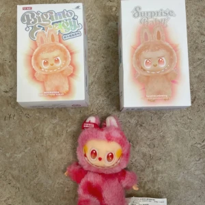Pop Mart Biginto Energy Surprise Baby Plush - Pop Mart Biginto Energy Surprise Baby är en samlarplush med unikt designad ansikte och rosa kanindräkt. Produkten är i mycket fint skick, komplett med originalförpackning. Perfekt för samlare eller som present. Inga synliga defekter eller slitage.