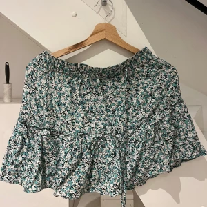 Blommig kortkjol från Zara - Säljer en blommig kortkjol från Zara i storlek M. Den är gjord i ett lätt och luftigt bomullsmaterial med elastisk midja och knytband framtill. Kjolen har också shorts innanför👌