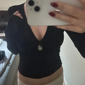 Svart croppad v-ringad topp - Svart långärmad topp med v-ringning och croppad passform. Toppen har en dekorativ knapp framtill och är figurnära. Perfekt för dig som gillar stilrena och enkla plagg med en liten twist. Materialet känns mjukt och stretchigt.